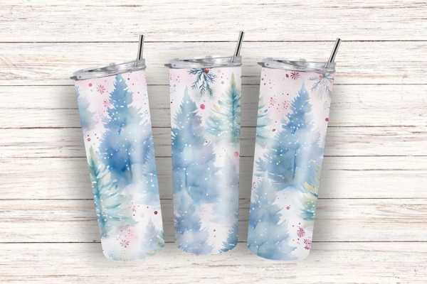 Drei Thermobecher mit aquarelliertem Winterdesign, das blaue Tannenbäume und zarte rote Akzente zeigt, auf einem rustikalen weißen Holzuntergrund arrangiert.